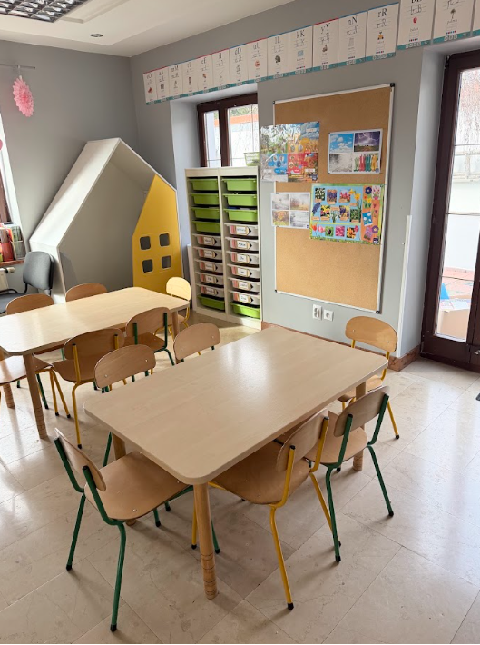 Sala dydaktyczna z domkiem, stolikami i tablicą prac dzieci